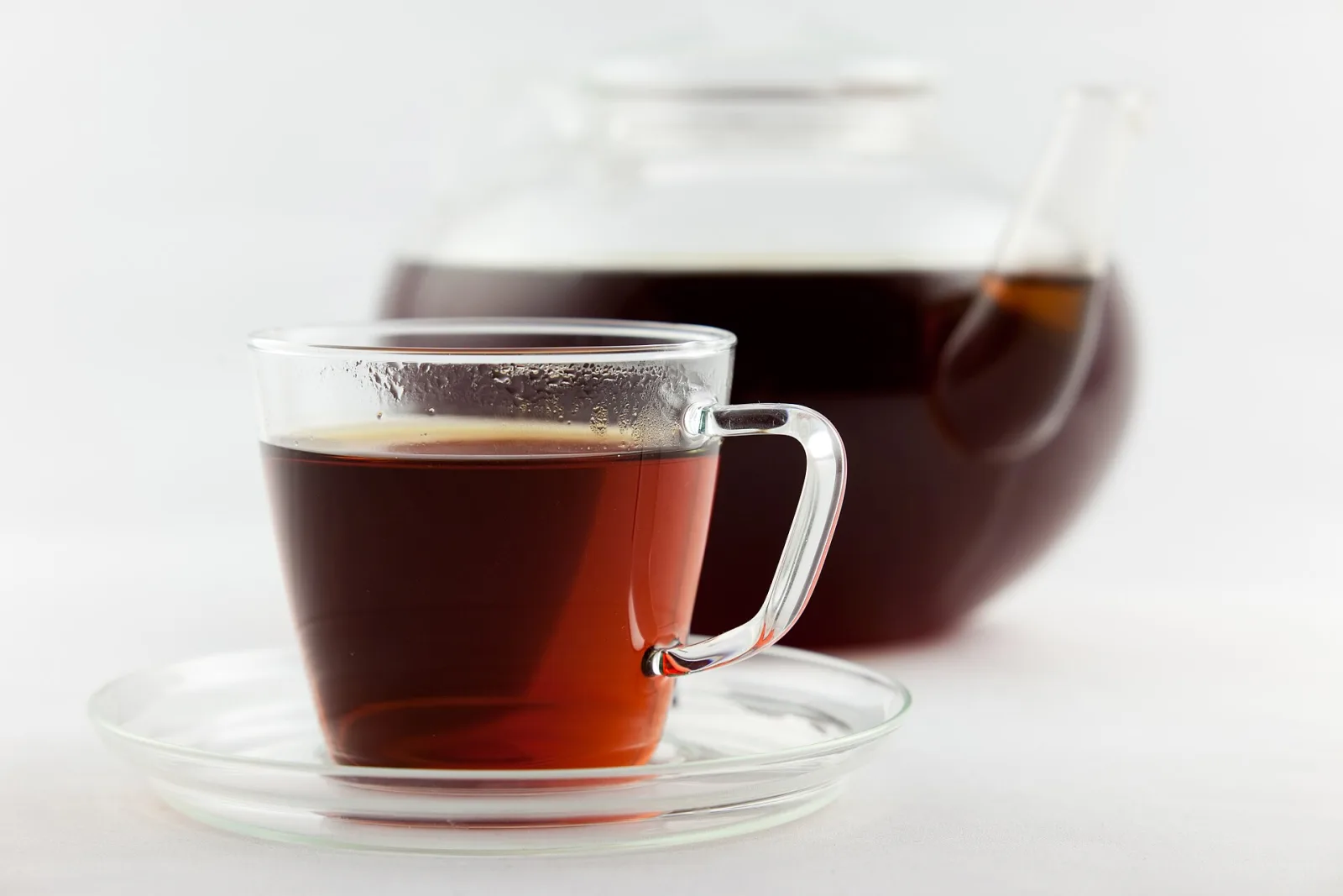 Tasse en verre de rooibos infusé, de couleur rouge ambré, devant une théière