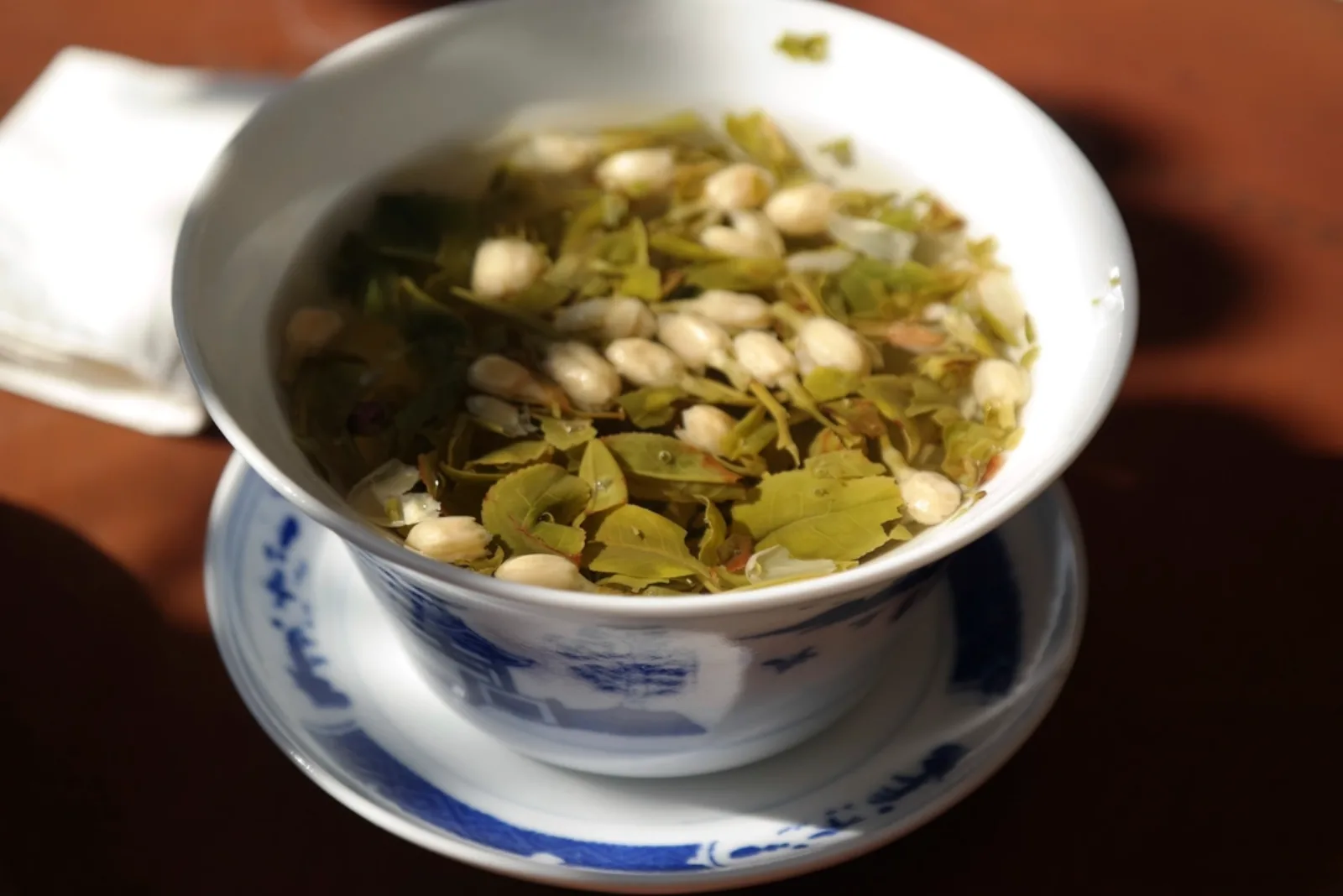 Bol en porcelaine rempli de feuilles de thé vert et de boutons de jasmin en cours d'infusion