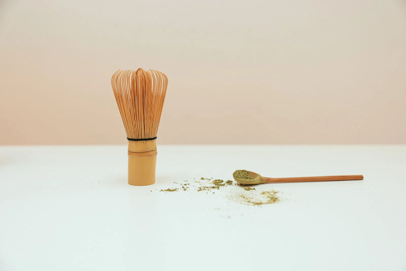 Fouet à matcha en bambou posé debout, à côté d'une cuillère en bambou chargée de poudre