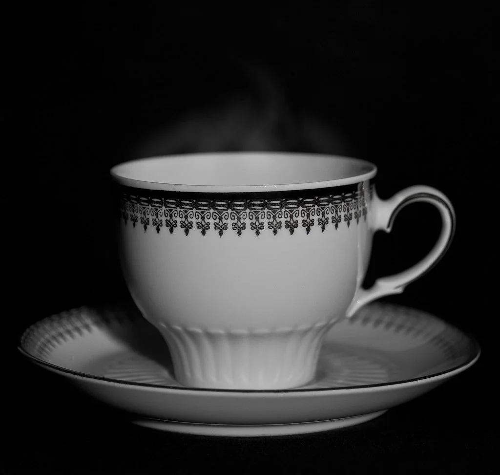 Tasse de thé noir fumante et sa soucoupe en porcelaine, sur fond sombre