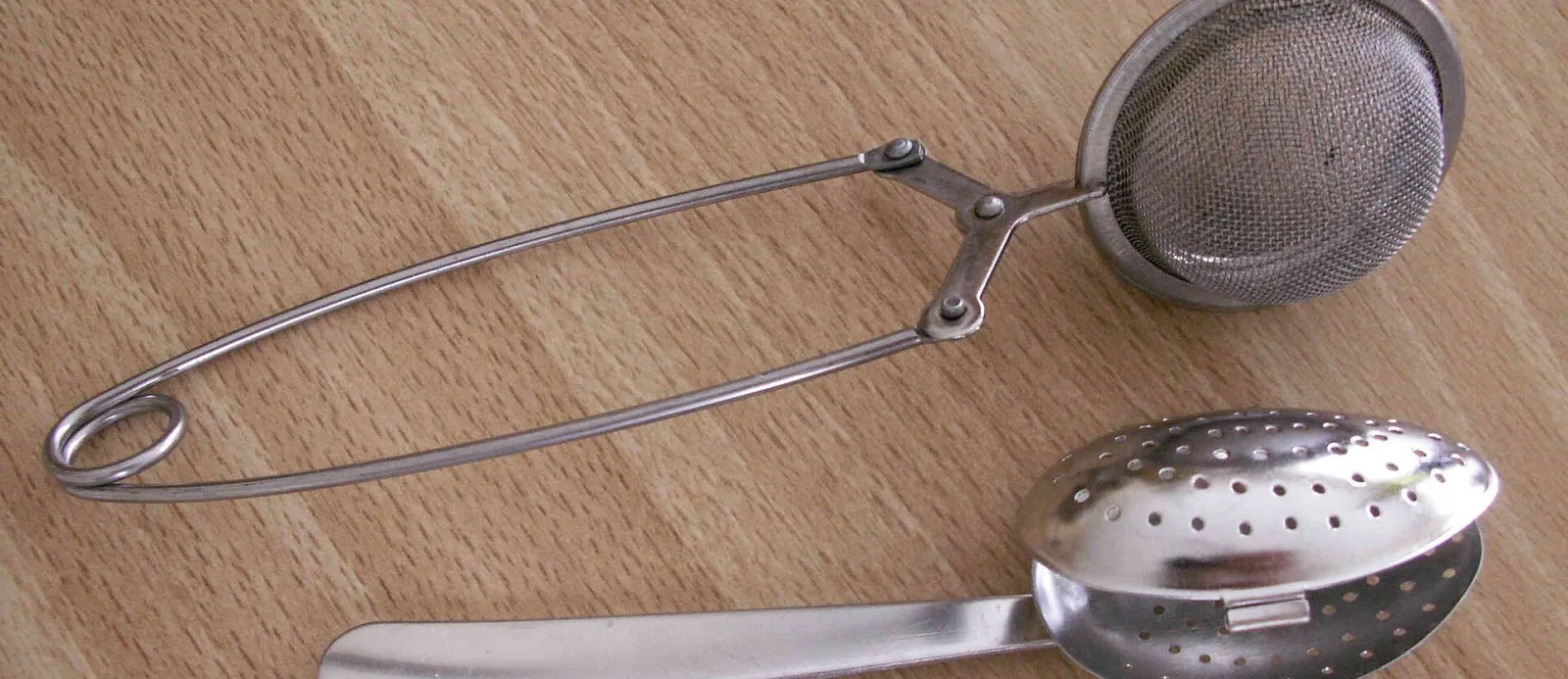 Pince-boule à thé en inox et cuillère-infuseur perforée posées sur une table