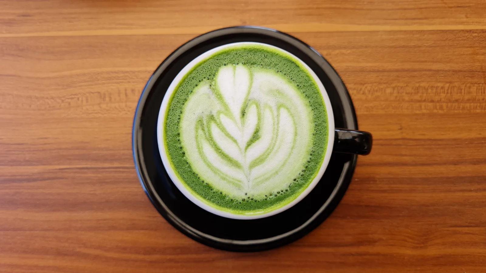 Matcha latte vu du dessus dans une tasse noire, avec un motif de rosetta dans la mousse de lait