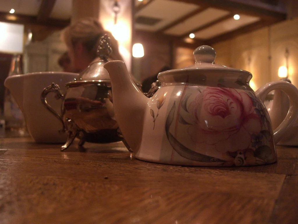 Théière fleurie et service à thé posés sur une table en bois, dans la lumière chaude d'un salon de thé