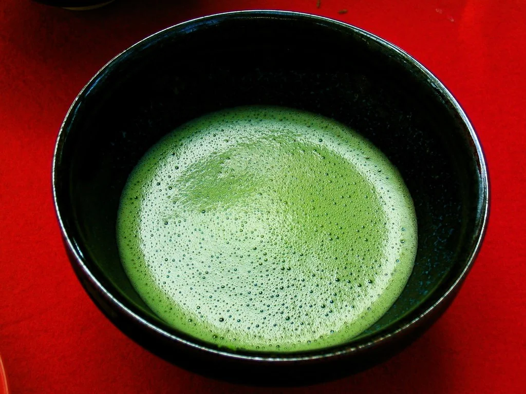 Bol de matcha fraîchement battu, mousse verte en surface, sur un tissu rouge
